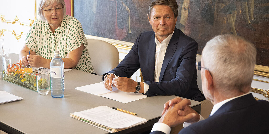 Bundespräsident Alexander Van der Bellen sitzt mit Angela Köppl und Wolfgang Anzengruber am Besprechungstisch in seinem Büro
