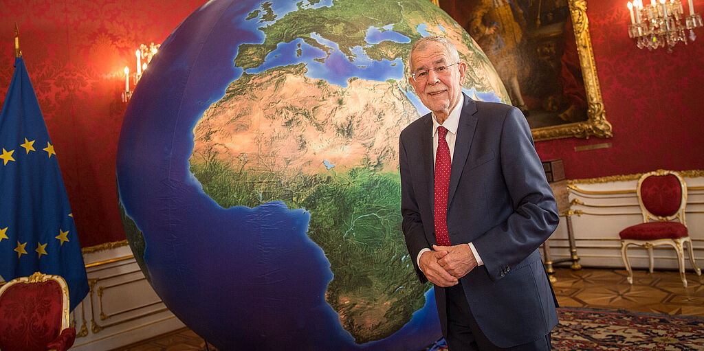 Bundespräsident Alexander Van der Bellen steht vor eine großen Erdkugel im Maria Theresien Zimmer der Präsidentschaftskanzlei