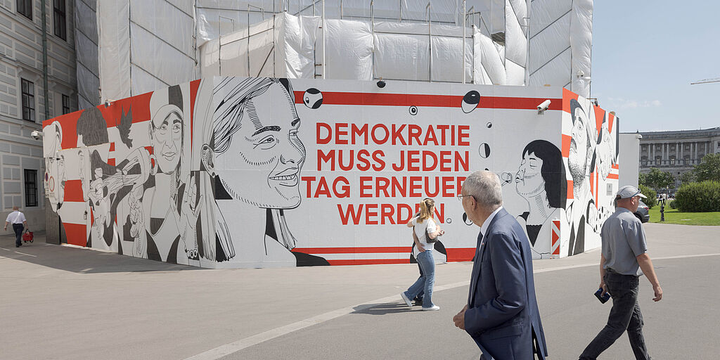 Bundespräsident Alexander Van der Bellen schaut sich die künstlerische Gestaltung der Baustellenverkleidung an