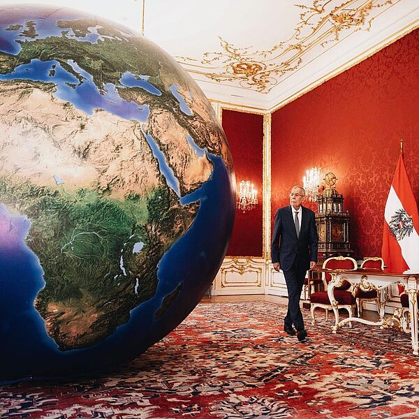 Alexander Van der Bellen geht an einer riesigen Erdkugel im Maria Theresien Zimmer vorbei