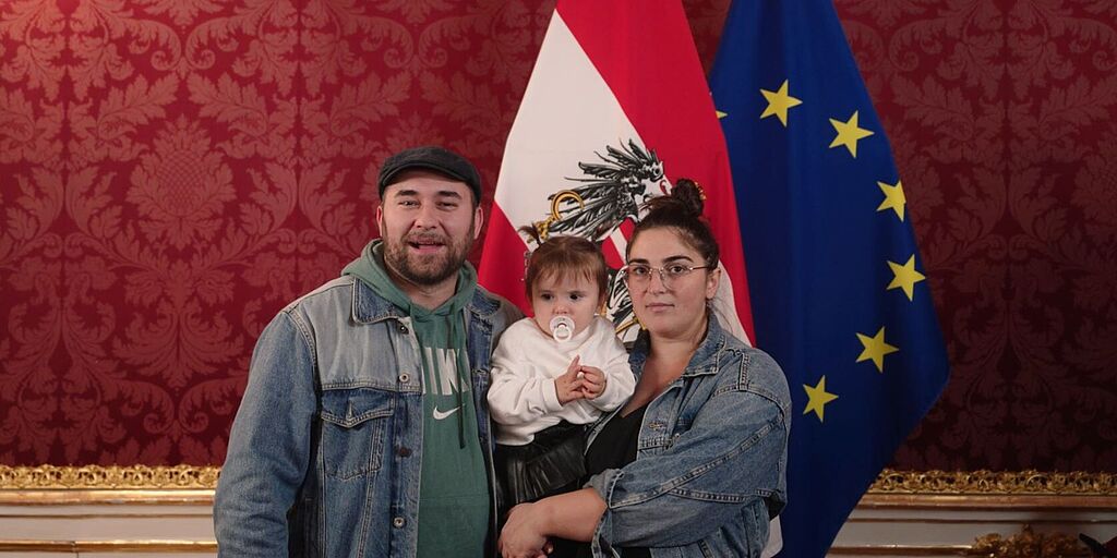 Eine Familie steht vor der österreichischen und der EU-Flagge